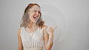 Cheerful young woman, proudly pointing to the side with a thumb-up, smiles happily on a pristine, isolated white background.