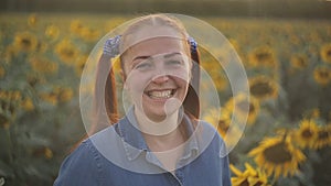 Cheerful young woman with red tails stands in the fields with sunflowers and smiles at the sunset. close-up portrait of