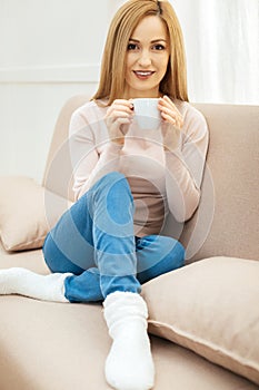 Cheerful young woman relaxing on the sofa with a cup of tea