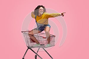 Cheerful young woman riding forward on shopping cart