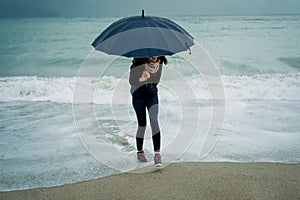 Cheerful Young woman runs from the wave with an umbrella in fro