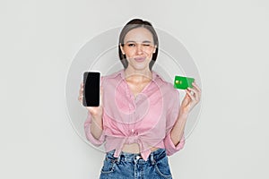 Cheerful young woman showing phone with blank screen, bank card