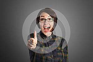 Cheerful young woman showing thumb up sign on grey background