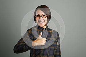 Cheerful young woman showing thumb up sign on grey background