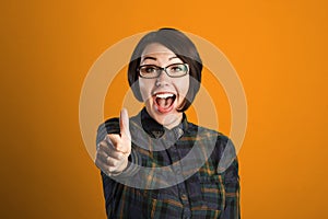 Cheerful young woman showing thumb up sign on orange background