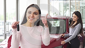 Cheerful young woman showing thumbs up holding car keys