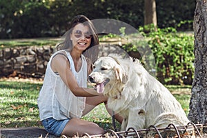 Portrait of cheerful young woman sitting with the dog in summer park