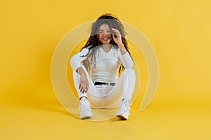 Cheerful young woman sitting on floor touching her hair while looking at camera