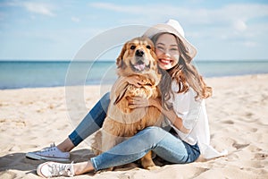 Cheerful young woman sitting and hugging her dog on beach