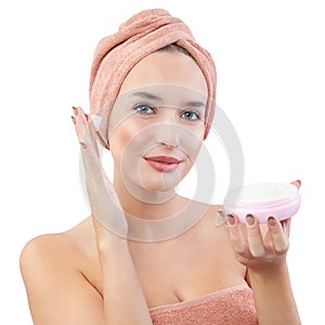 Cheerful young woman smiling, applying on face moisturizing skincare cream, lotion or mask for skin lifting and anti-aging, wears