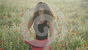 Cheerful young woman spinning in field of poppies on sunny summer day. Portrait of beautiful curly-haired Caucasian lady