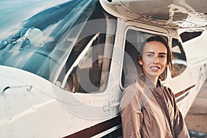 Cheerful young woman standing near airplane at airdrome