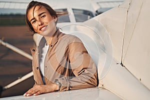 Cheerful young woman standing near plane at airdrome