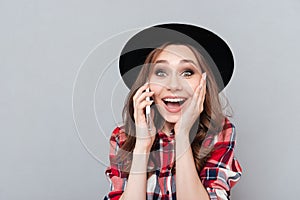 Cheerful young woman standing over grey wall talking by phone.