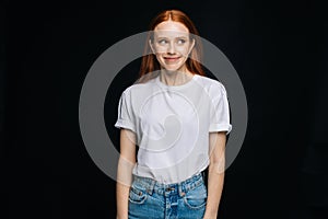 Cheerful young woman in T-shirt and denim standing posing on isolated black background,