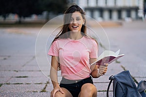 Cheerful young woman taking notes while sitting on steps otdoors