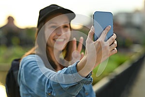 Cheerful young woman travel blogger waving hand, recording video vlog with smartphone