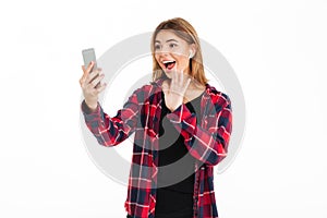 Cheerful young woman using mobile phone with earphones waving.