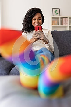 Cheerful young woman using mobile phone while relaxing on sofa at home