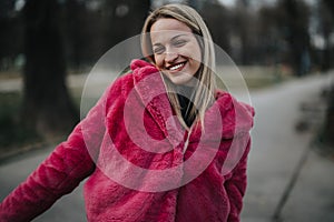 Cheerful young woman in vibrant pink jacket enjoying a chilly day outdoors