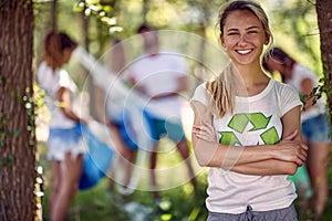 Cheerful young woman volunteer in nature. Group of people cleaning up forest or park doing charity work. Environmentalism, green,