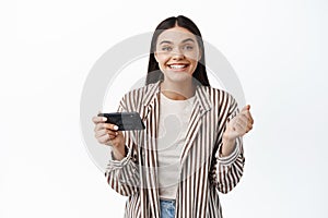 Cheerful young woman winning money on phone, achieve goal in smartphone app, holding mobile phone horizontally and say