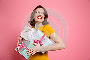 Cheerful young woman in yellow dress holding heap of presents