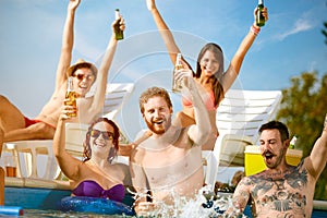 Cheerful youngsters group toasting with bottles of drink in piscine photo