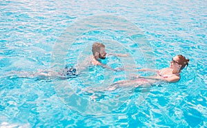 Cheerful youthful guy and lady resting while swimming pool outdoor. Couple in water. Guys do summer sephi