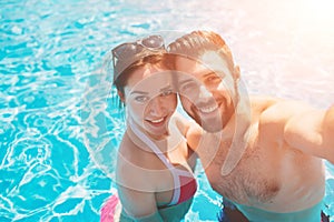 Cheerful youthful guy and lady resting while swimming pool outdoor. Couple in water. Guys do summer sephi