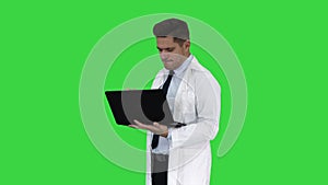 Cheerfull doctor with laptop laughing after giving a serious look to camera on a Green Screen, Chroma Key.