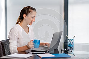 Cheerfull young business woman sitting at her desk and drinking tea. photo