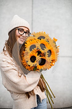 Cheerfully girl in knitted hat and sweater with a sunflowers near a wall photo