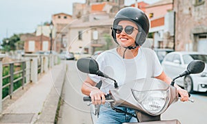 smiling woman in helmet and sunglasses fast riding the moto scooter on the Sicilian old town streets in the Forza d\' photo