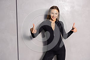 Cheerfully sporty woman thumb up, on gray wall background