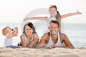 parents with two kids lying on the beach.