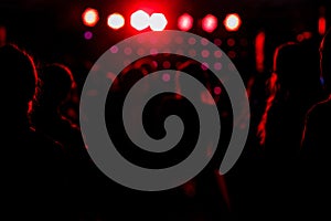 cheering crowd in front of bright red stage lights. Silhouette image of people dance in disco night club or concert at a