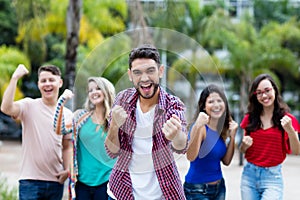 Cheering hipster young adult with beard showing thumb up with group of friends