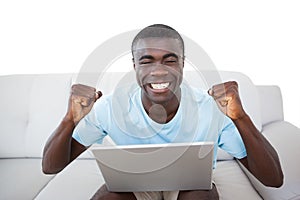 Cheering man sitting on couch using laptop
