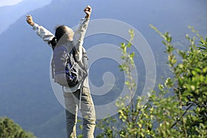 Cheering woman hiker open arms at mountain peak