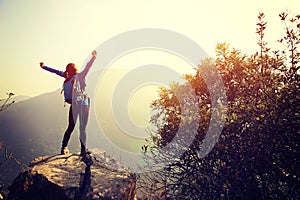 Cheering woman hiker open arms at mountain peak