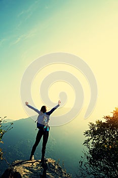 Cheering woman hiker open arms at mountain peak