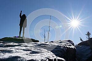 Cheering woman hiker open arms at mountain peak backlit with heavy lensflare and ice crystalls in the foreground.