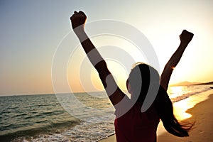 Cheering woman open arms to sunrise at sea