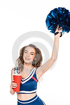 Cheerleader girl in blue uniform holding pompom and soda in paper cup isolated on white