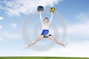 Cheerleader girl jumps with pom poms in meadow