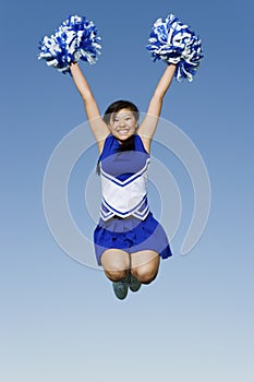 Cheerleader With Pompoms In Midair Against Sky