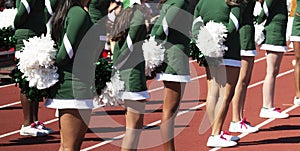 Cheerleaders in green uniforms holding white pom poms behind their backs