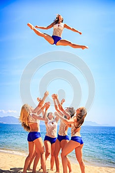 Cheerleaders perform Toe Touch Toss on beach