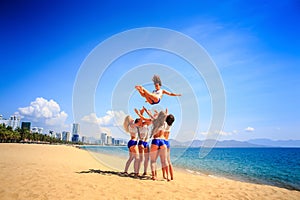 Cheerleaders perform tumbling toss on beach against azure sea